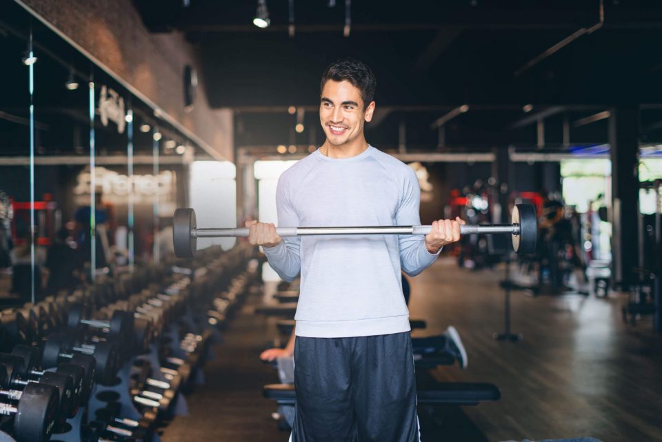 Junger Mann trainiert im Fitnessstudio mit einer Hantel.